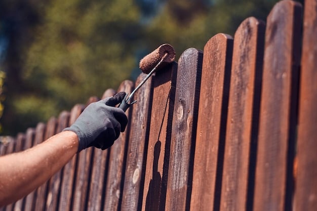 Man in protective gloves is painting wooden fence in bright summer day.